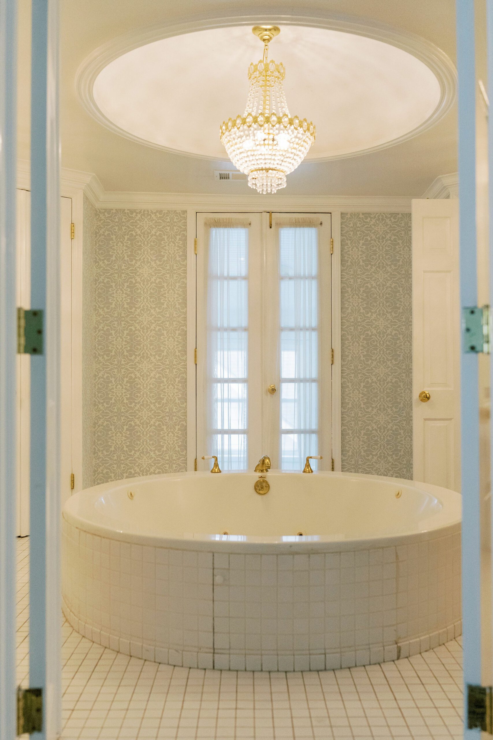 A white tile bathroom and an elegant chandelier. The centerpiece is a huge tub big enough to fit two people The Bride and the groom kissing at the alter at The Matthews house
